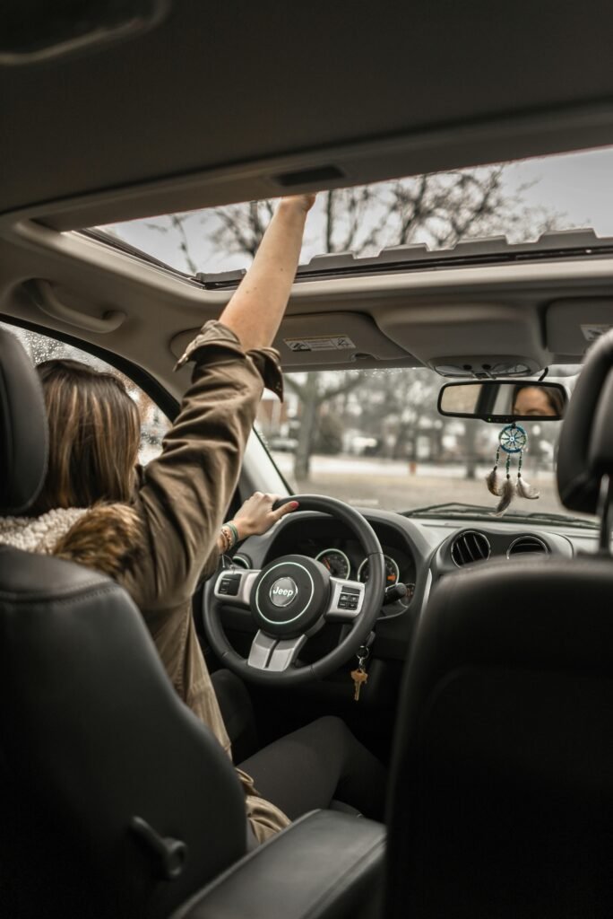 A young woman enjoying a drive with the sunroof open, showing car interior detail.